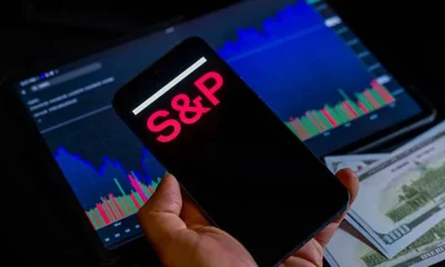 The s p global logo displays on a mobile screen and the dow jones industrial average closes.webp